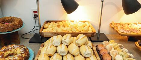 A variety of baked goods displayed on wooden trays, with two black desk lamps illuminating the scene.