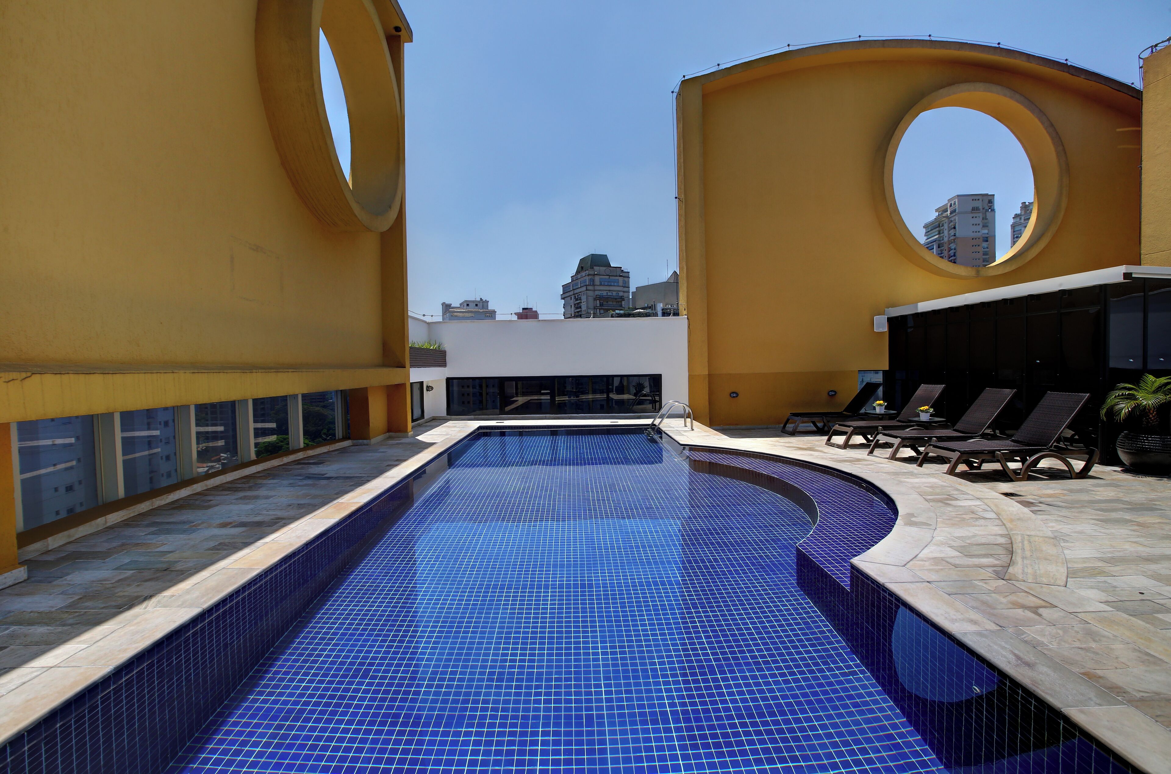 Una piscina en la azotea con baldosas azules, tumbonas y vistas al horizonte de la ciudad.