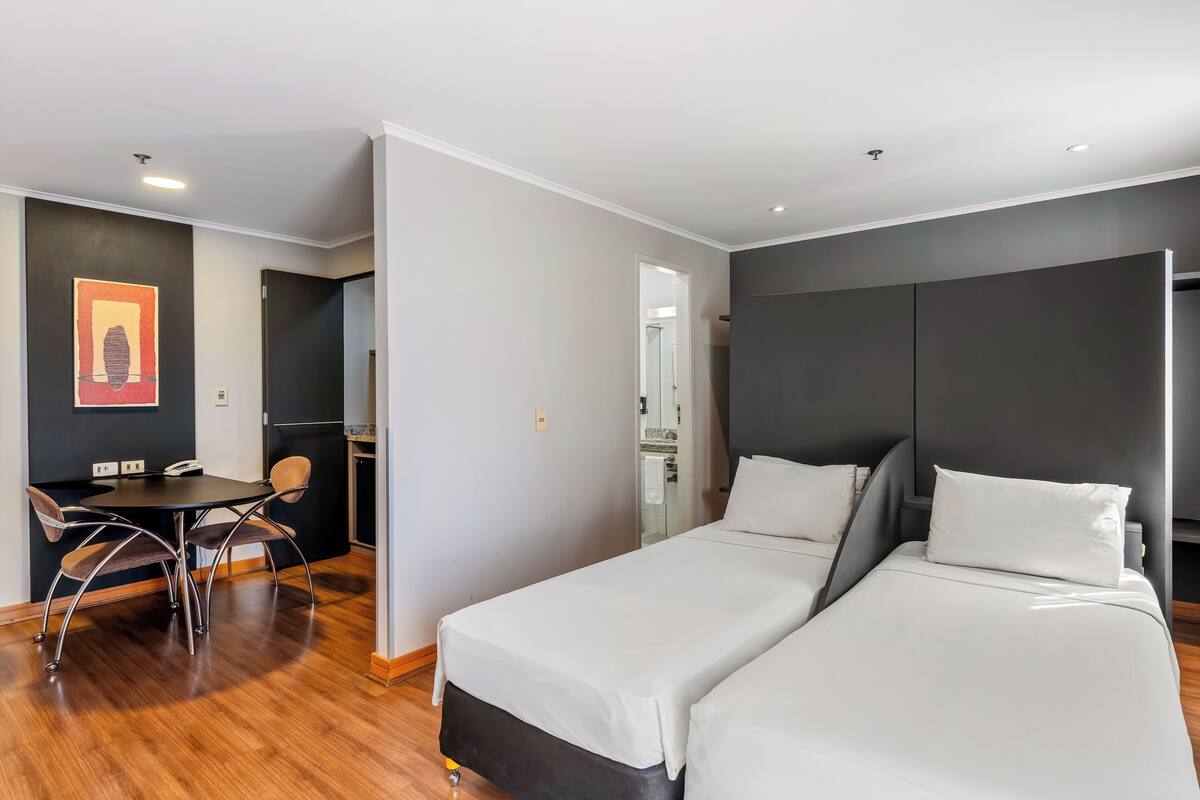 Een moderne hotelkamer met twee enkele bedden, een eettafel en een apart zithoekje.