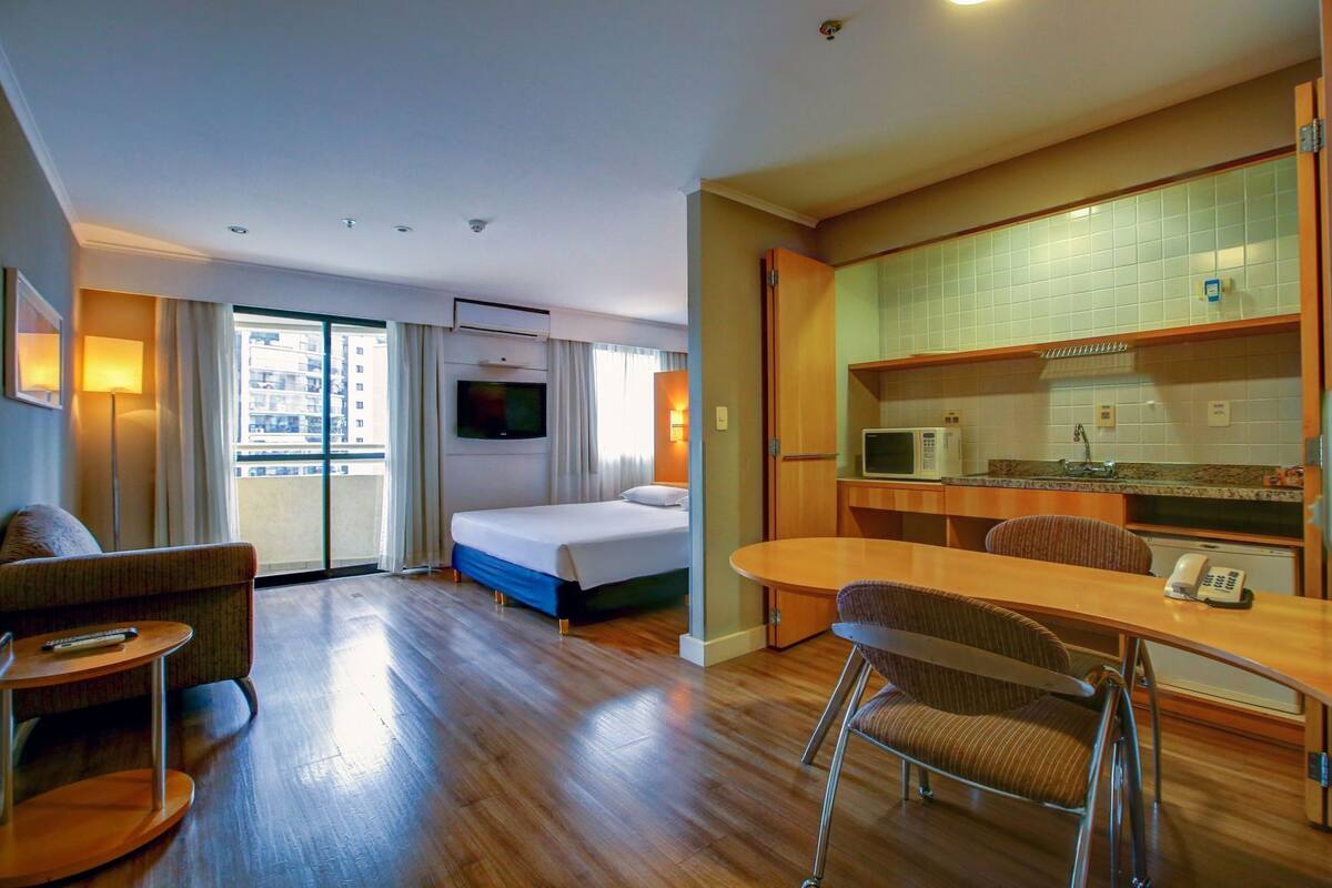 Een hotelkamer met een bed, een televisie, een eethoek en een kitchenette.