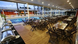 A restaurant with a pool view, wooden tables, and chairs. - Hotel Premium Campinas (Campinas)