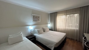 A hotel room with two beds, a nightstand with a lamp, a framed picture on the wall, and a window with curtains. - Hotel Premium Campinas (Campinas)
