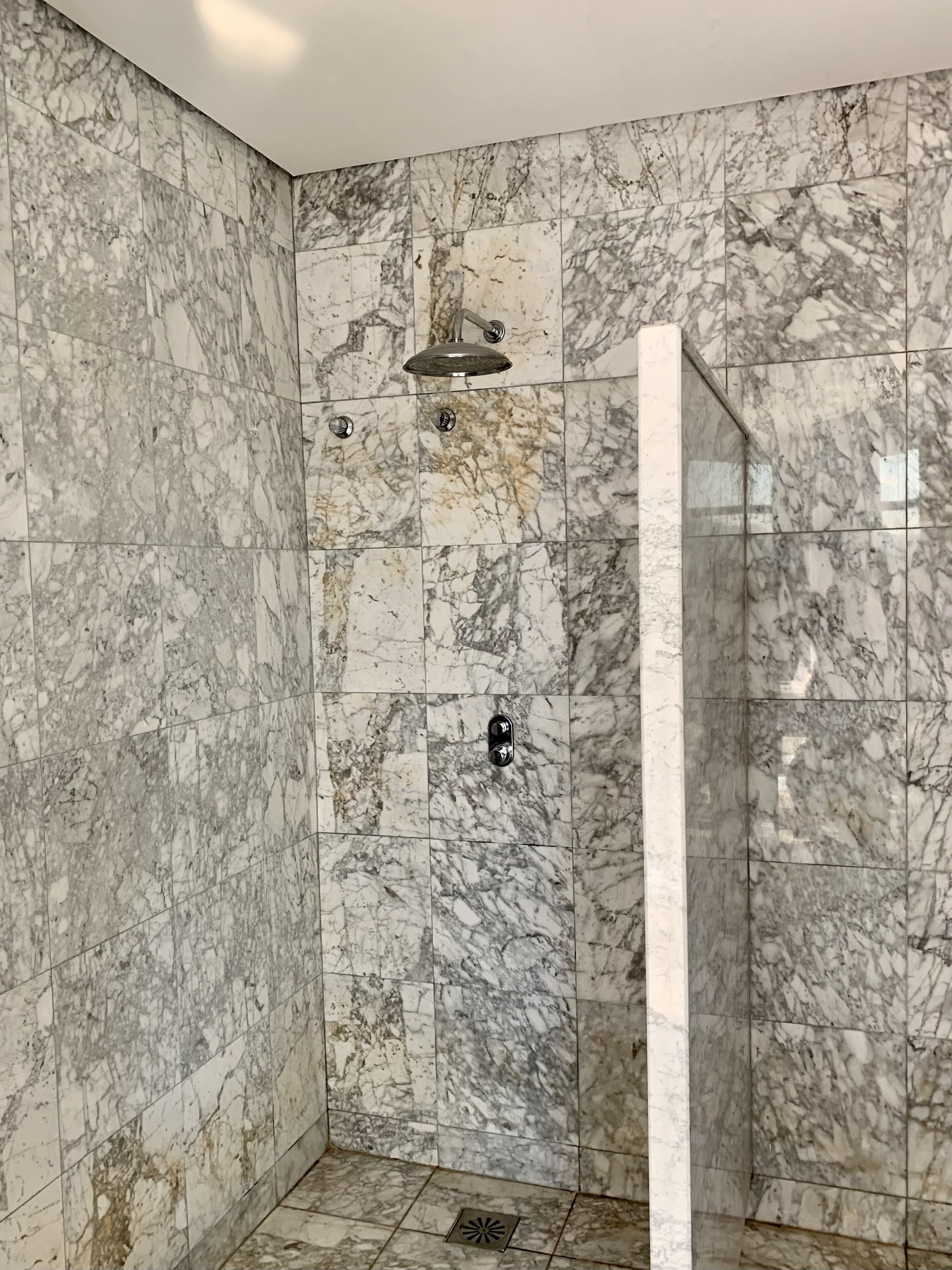 A bathroom with marble walls and a shower area.
