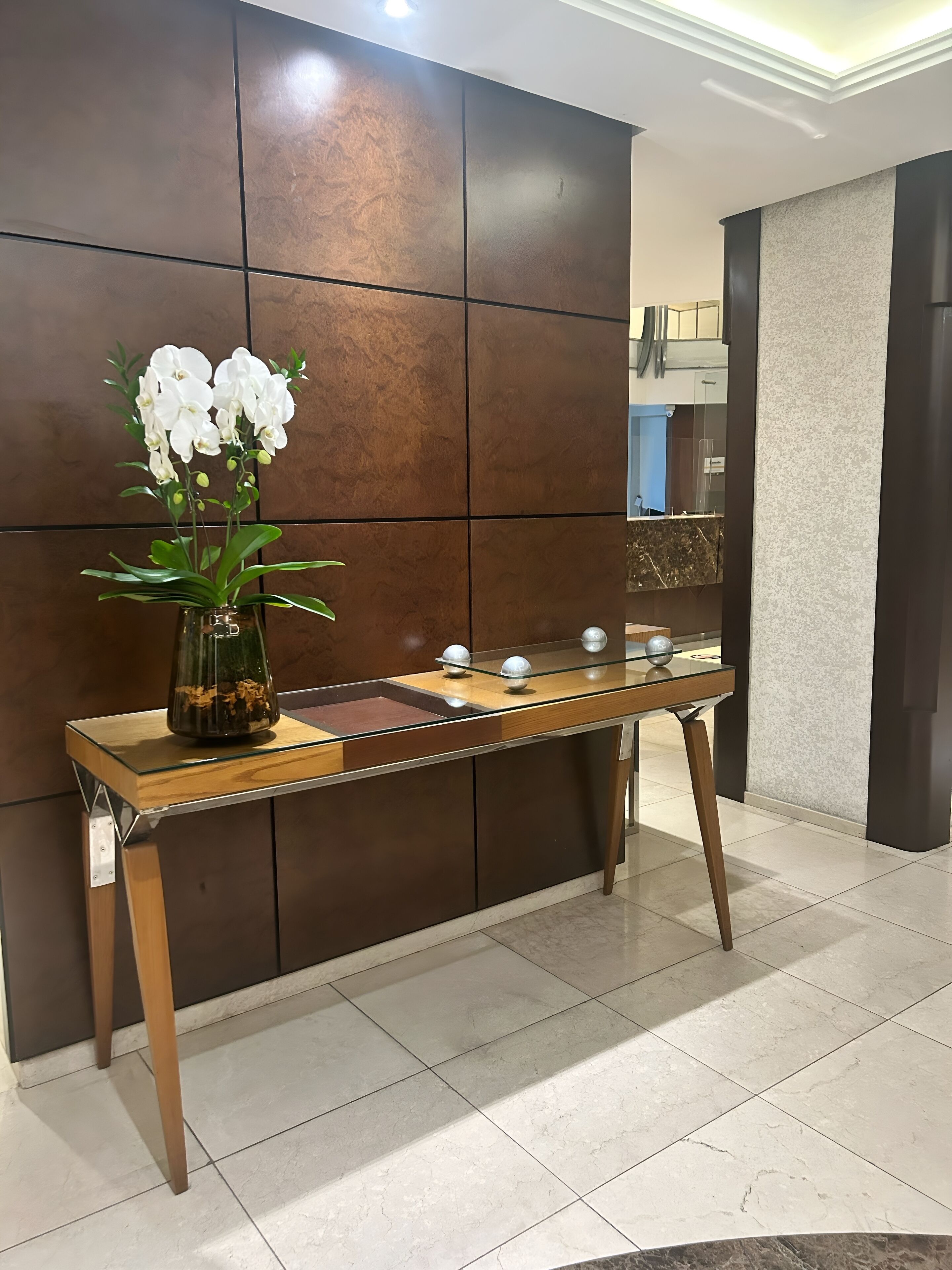 A reception desk with a vase of white orchids, a marble-topped table, and a modern wall with a mirror.