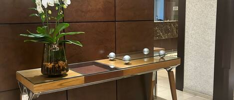 Un mostrador de recepción con un jarrón de orquídeas blancas, una mesa de mármol y una pared moderna con un espejo.