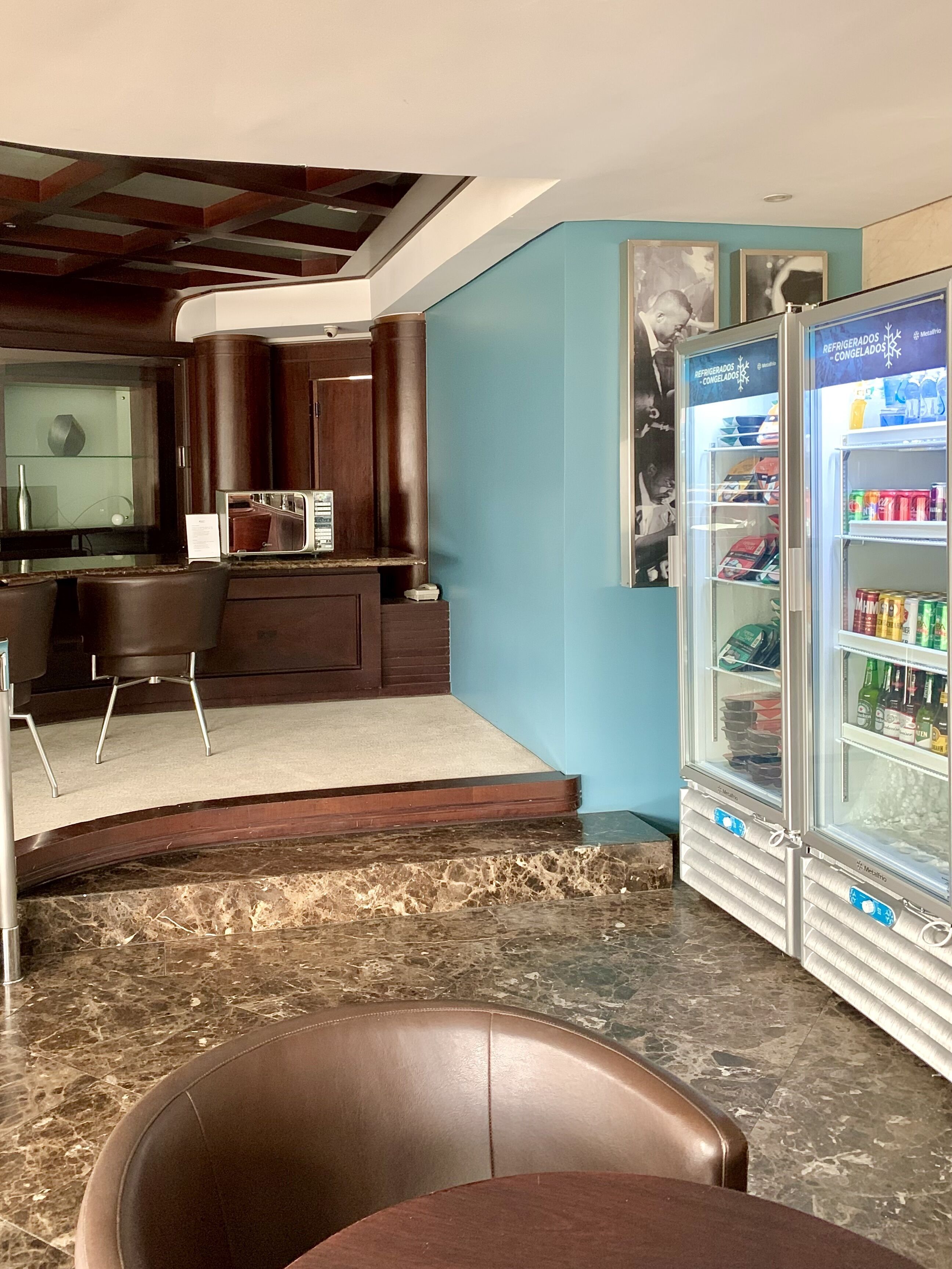 A modern bar area with a marble countertop, a seating area with a brown leather chair, and a minibar with a variety of beverages.