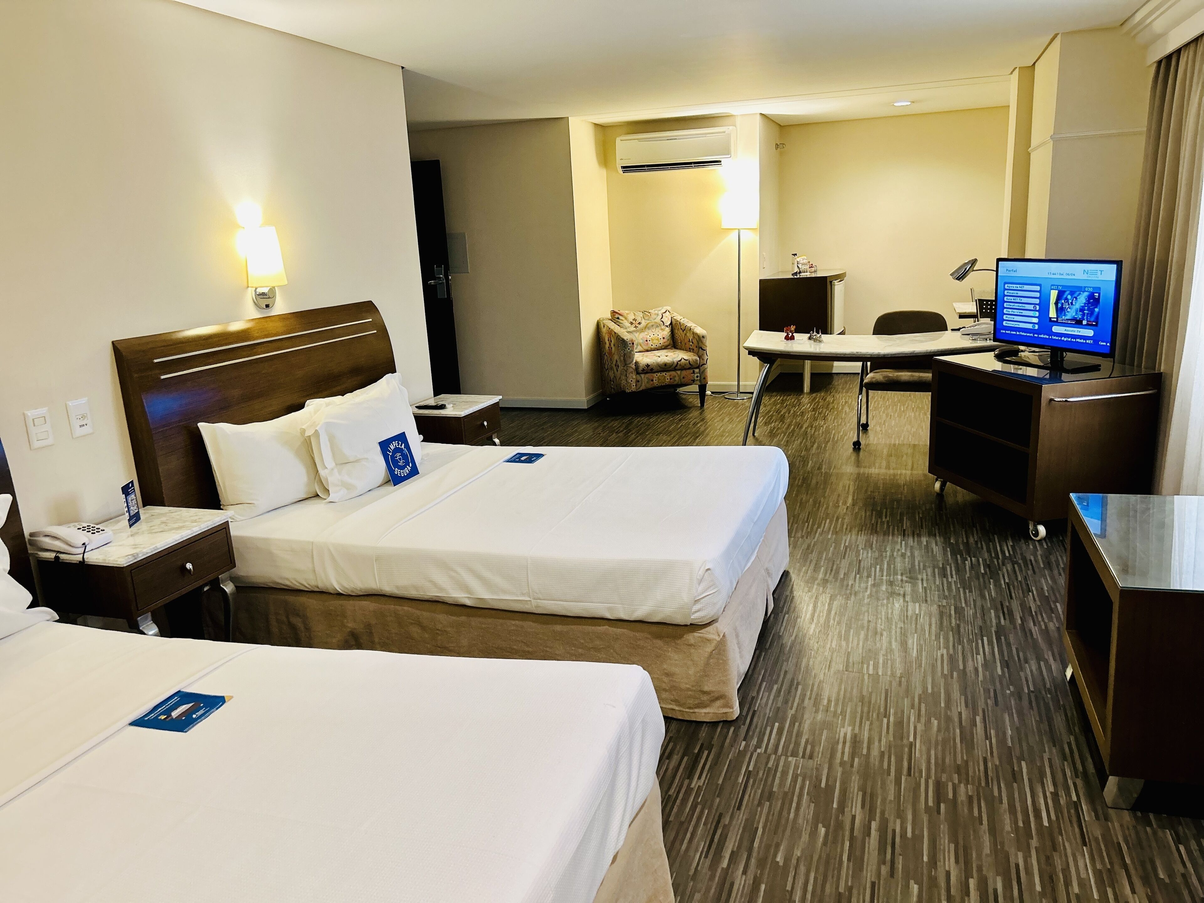 Habitación de hotel con dos camas, un escritorio, una silla, un televisor y un aire acondicionado.