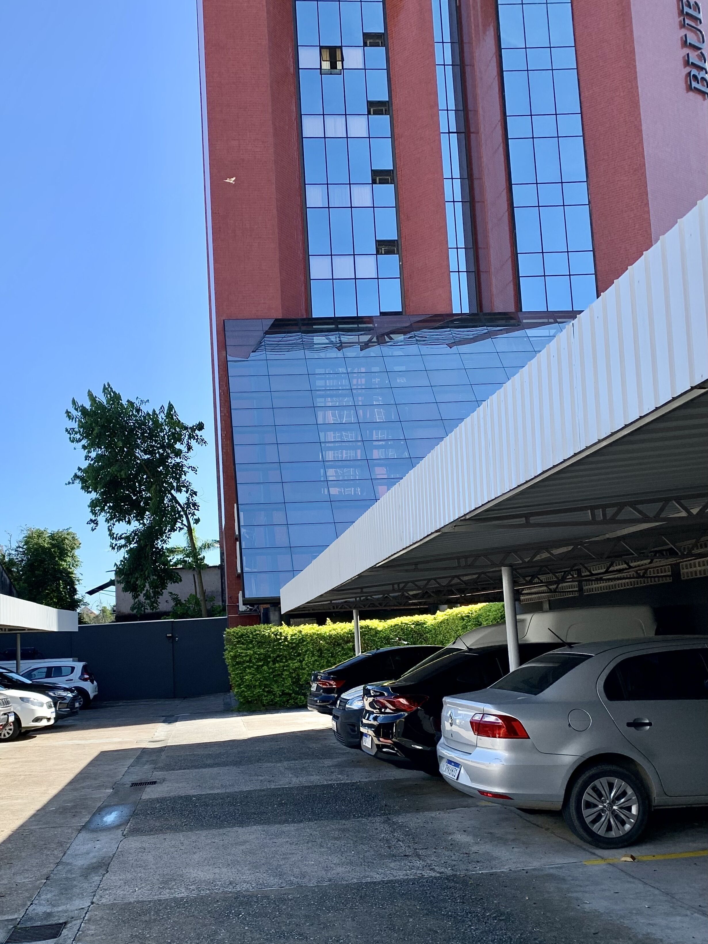 A parking area with several cars, a building with a reflective glass facade, and a clear blue sky.