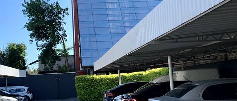 A parking area with several cars, a building with a reflective glass facade, and a clear blue sky.