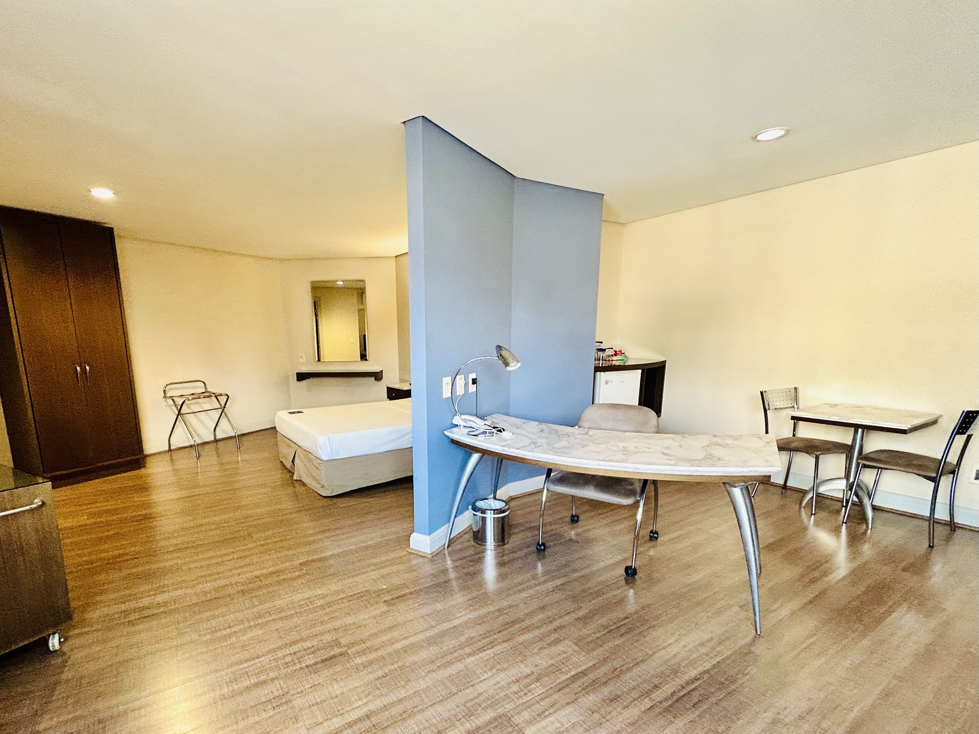 Ein modernes Hotelzimmer mit Bett, Schreibtisch, Stuhl, kleinem Tisch und Kleiderschrank.