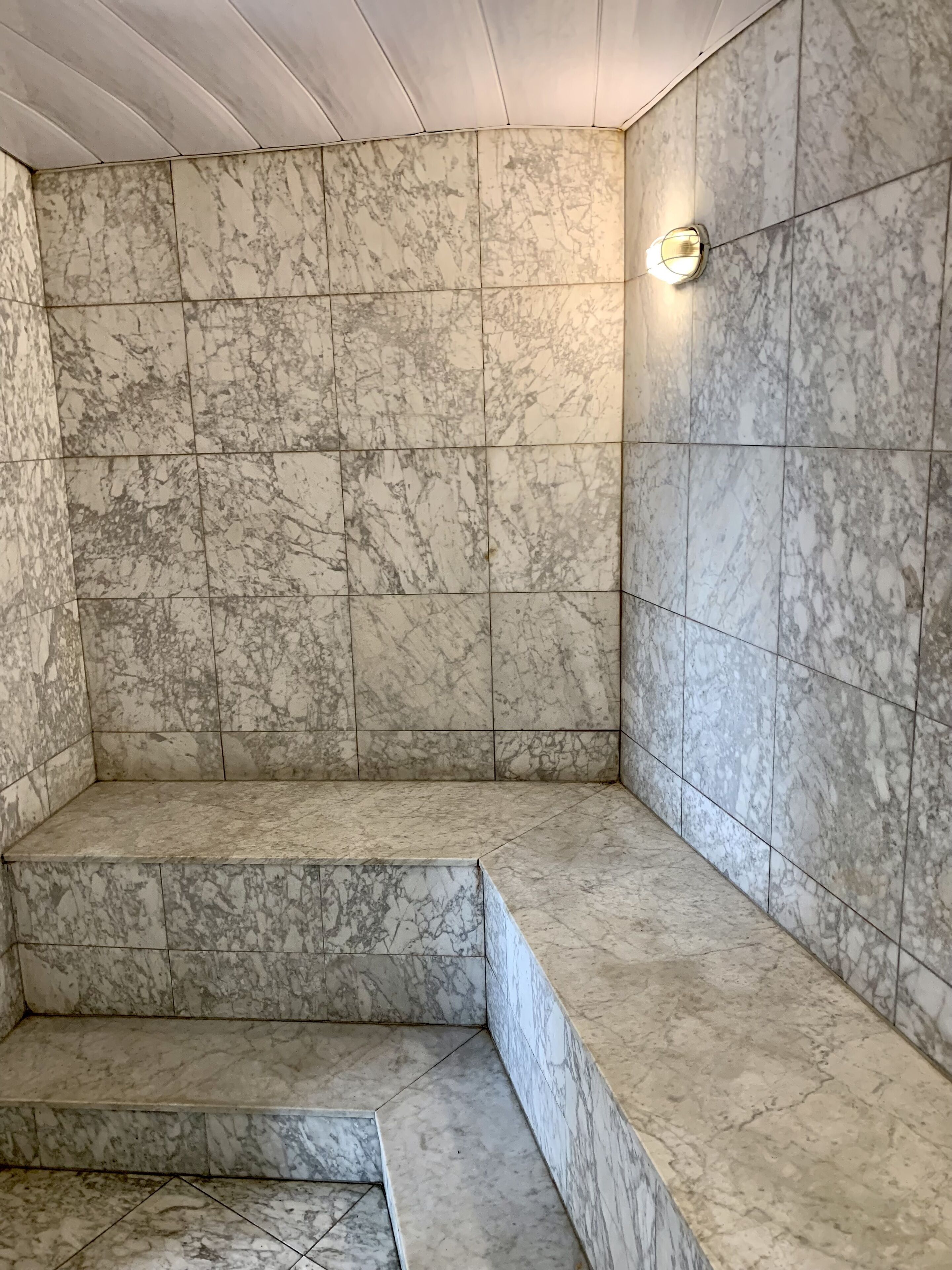 Ein Badezimmer mit Marmorfliesen, einer integrierten Sitzbank und einer Wandleuchte.