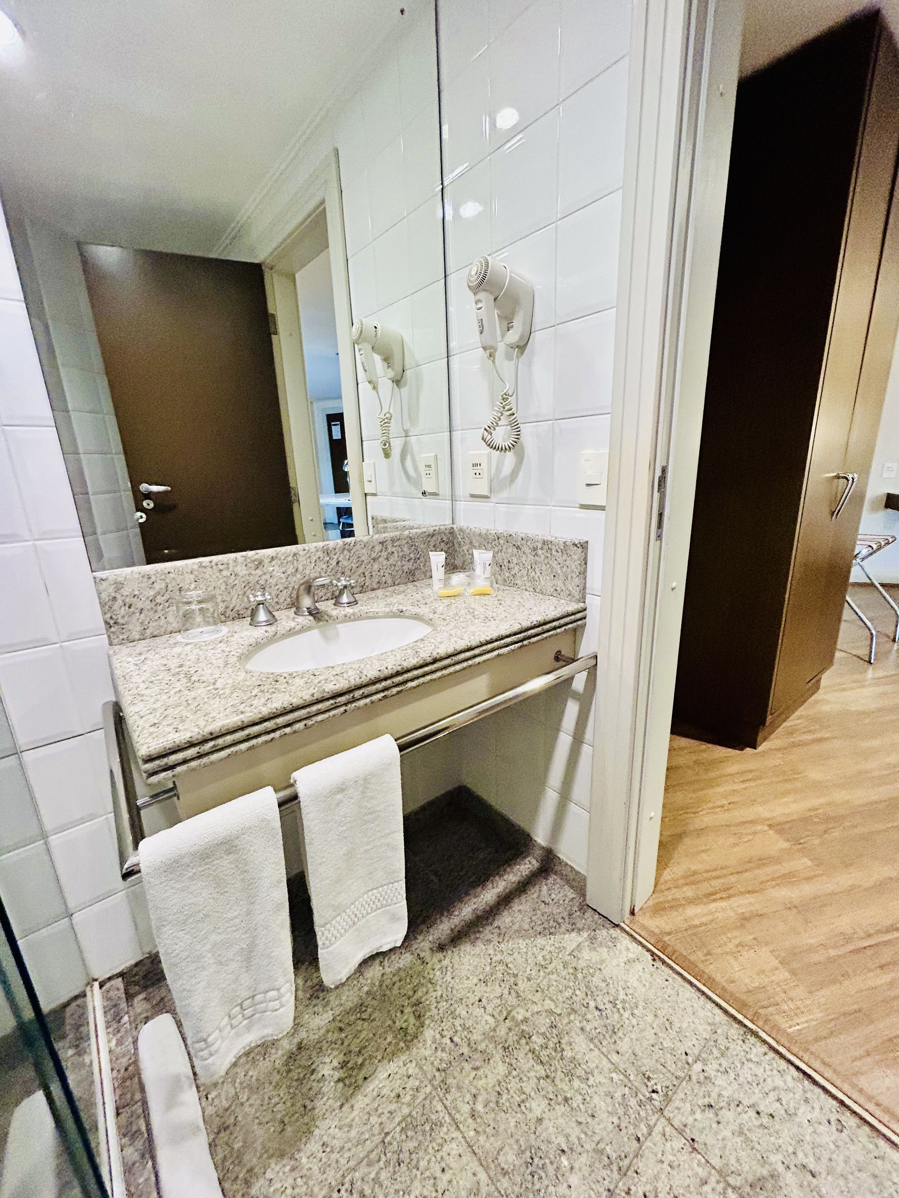 Une salle de bain moderne avec deux lavabos, un miroir et un sèche-cheveux fixé au mur.