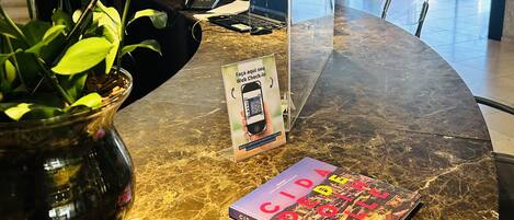 A marble reception desk with a laptop, a QR code sign, a book titled 'CIDADE DE JOINTVILLE', and a vase with red flowers.