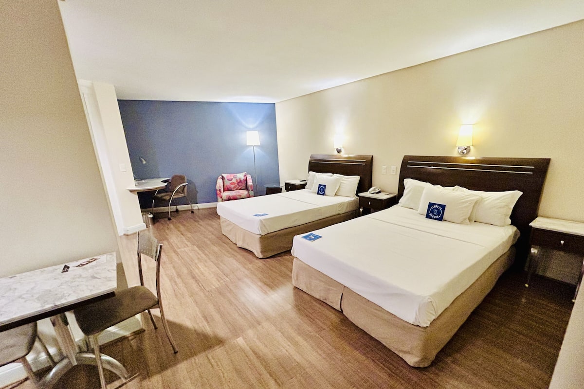 A hotel room with two beds, a desk, a chair, and a small table.