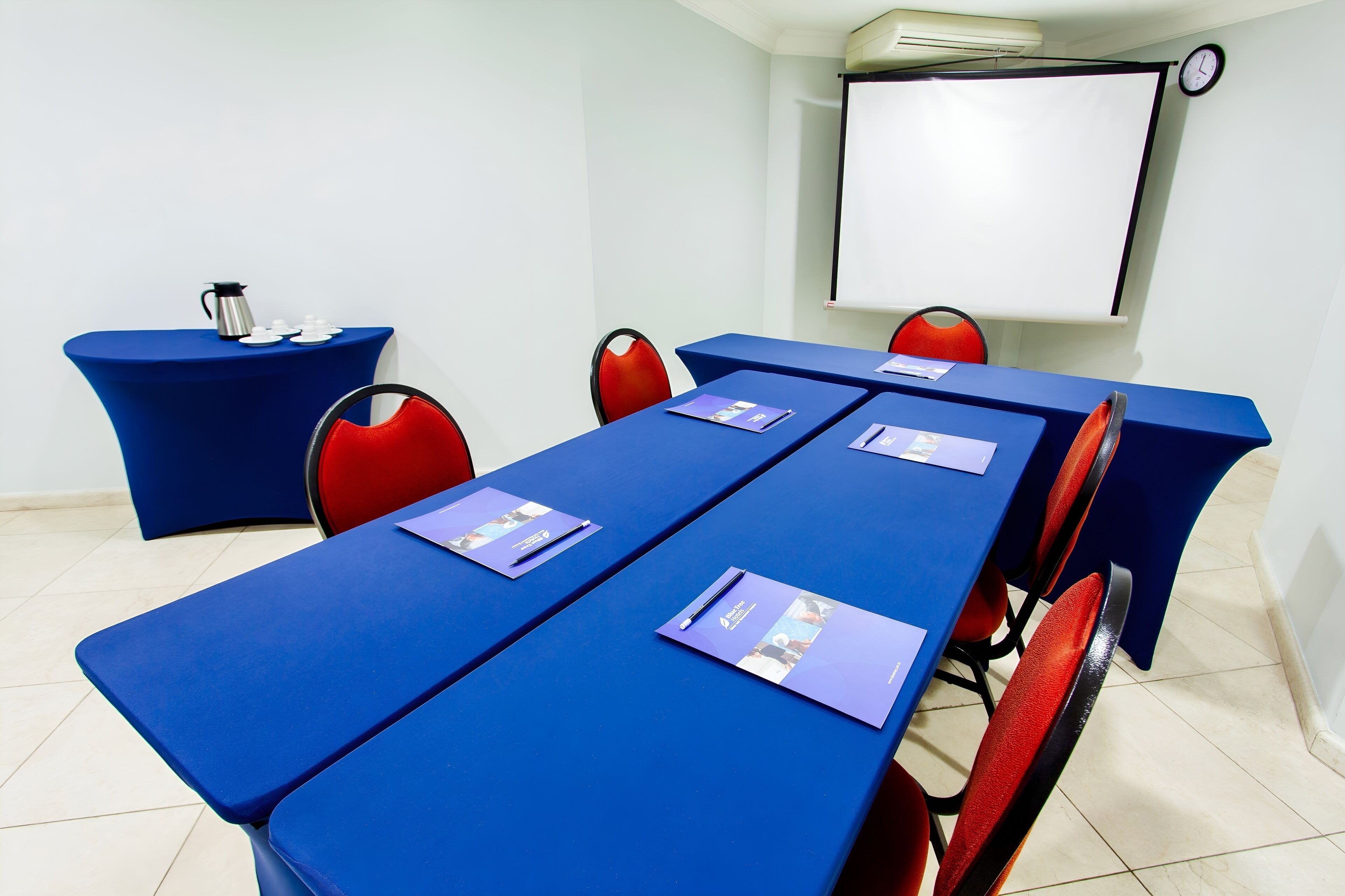 Een vergaderruimte met een lange tafel, rode stoelen en een blauwe tafelkleed.