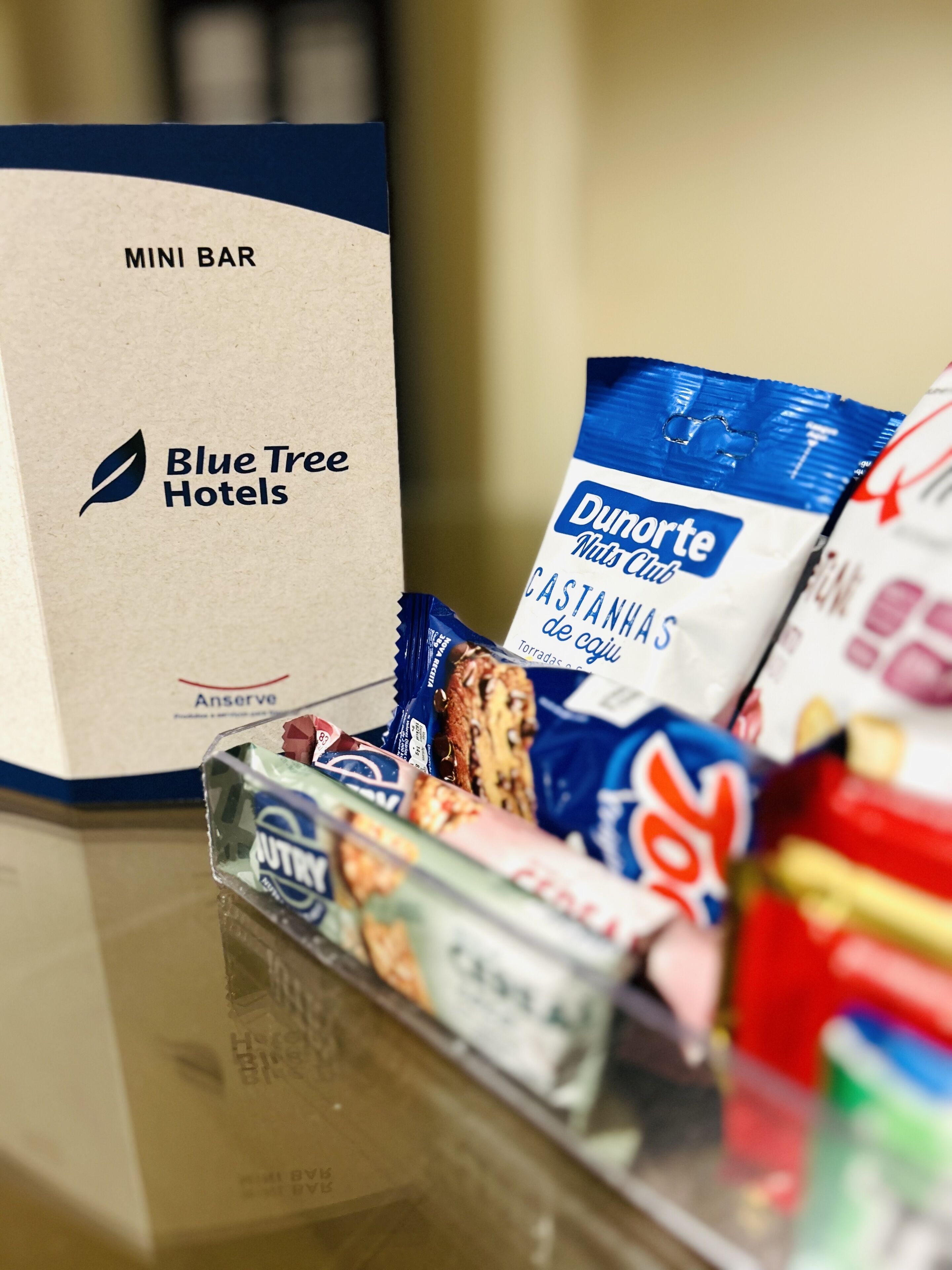 Un petit coin bar avec une enseigne indiquant « Blue Tree Hotels » et divers en-cas, notamment un paquet de noix de la marque Dulorte Nuts Club.