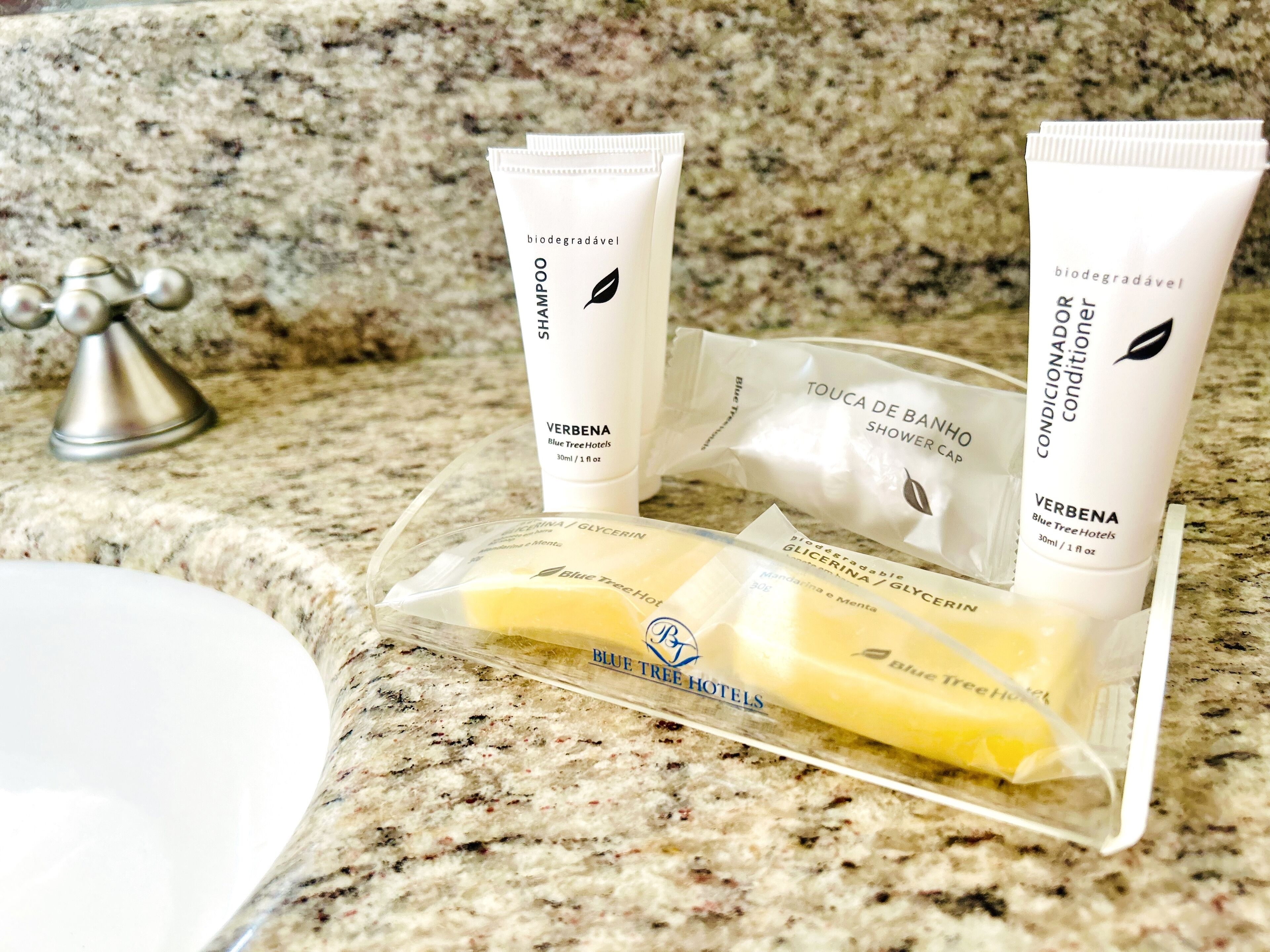 A bathroom counter with toiletries including a shampoo and conditioner tube, a shower cap, and a bar of soap.