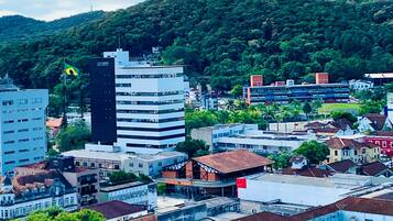 Un paisaje urbano con una mezcla de edificios modernos y tradicionales, un edificio blanco destacado y una colina con vegetación densa al fondo.