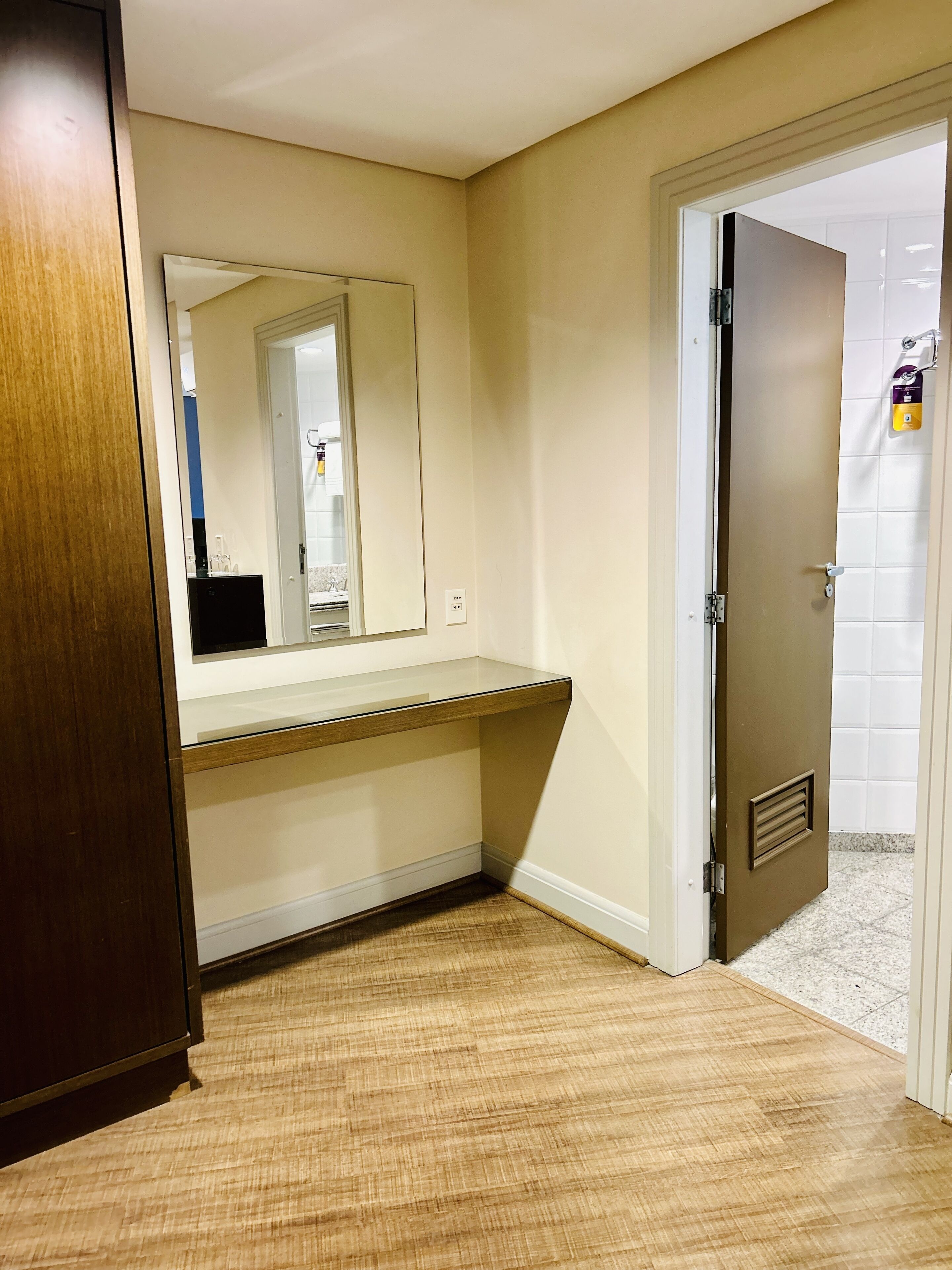 Een badkamer met een houten wastafelmeubel, een spiegel en een deur naar de douche.