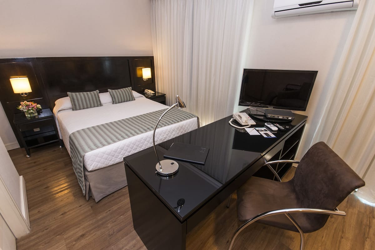 A hotel room with a bed, a desk with a chair, a television, and a phone.