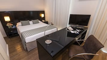 A hotel room with a bed, a desk with a chair, a television, and a phone.