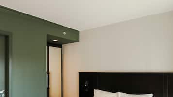 A modern hotel room with a large bed, a dark headboard, and a green accent wall.