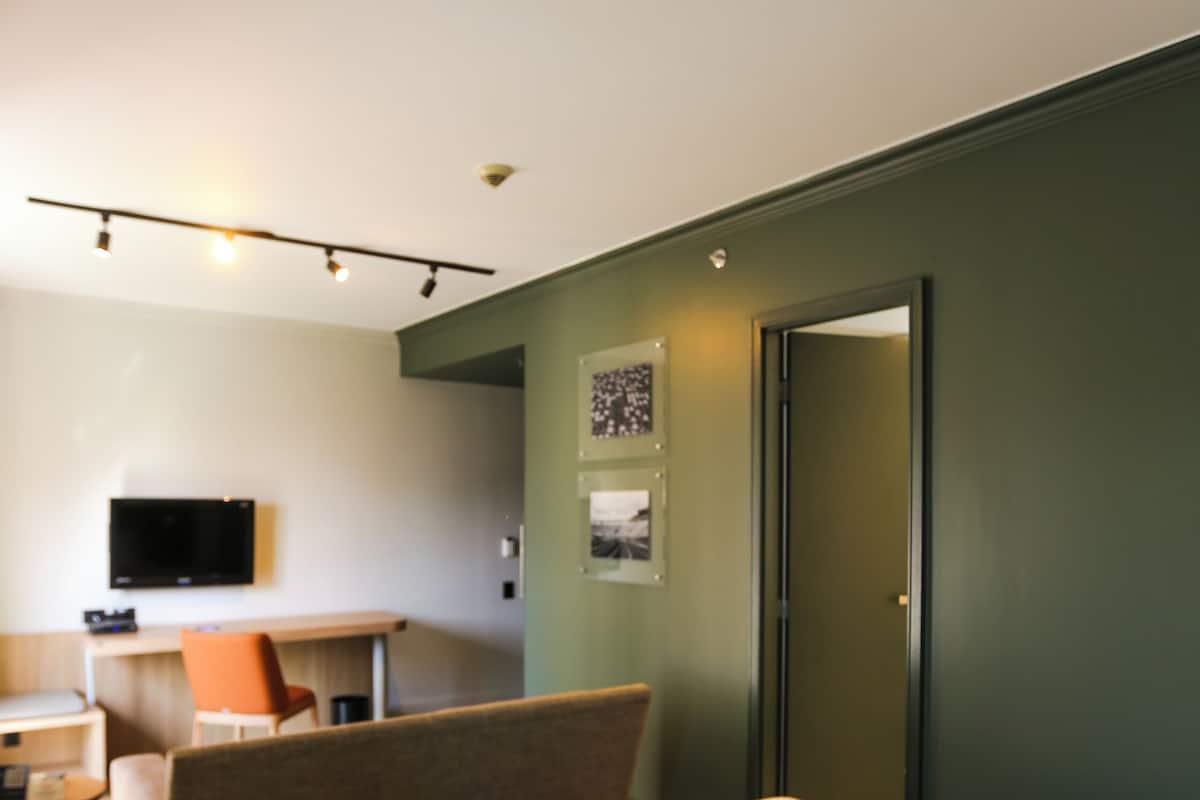 A hotel room with a bed, a desk, a chair, and a television on the wall.