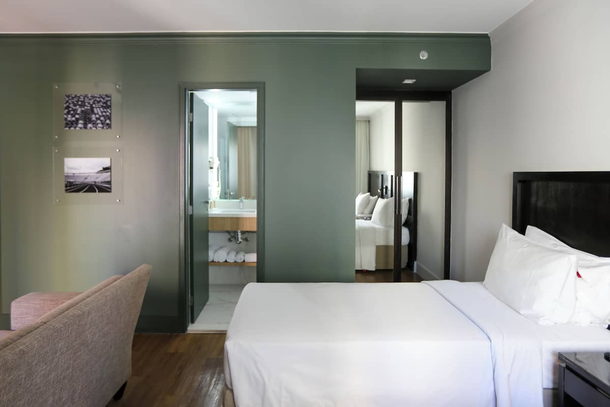 A hotel room with a bed, a chair, a bathroom with a sink, and a mirror.