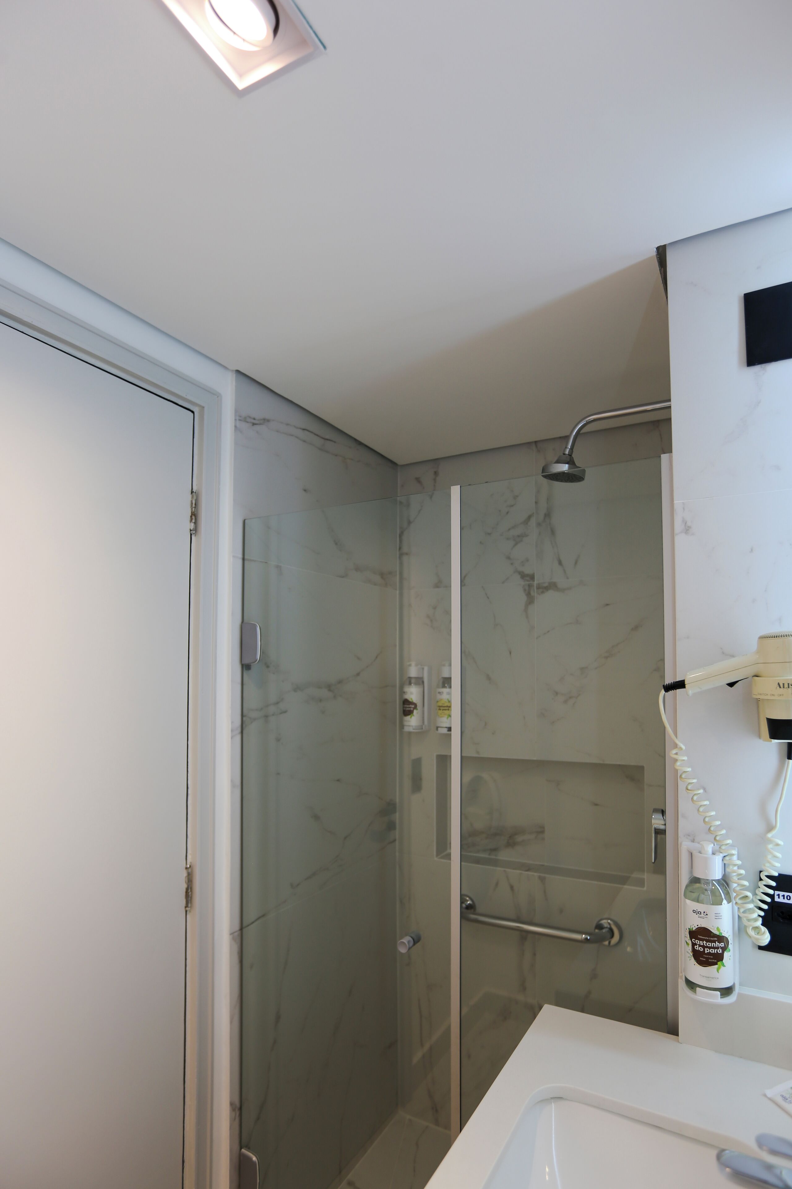 Un baño moderno con cabina de ducha de vidrio, un lavamanos blanco y un secador de pelo en la pared.