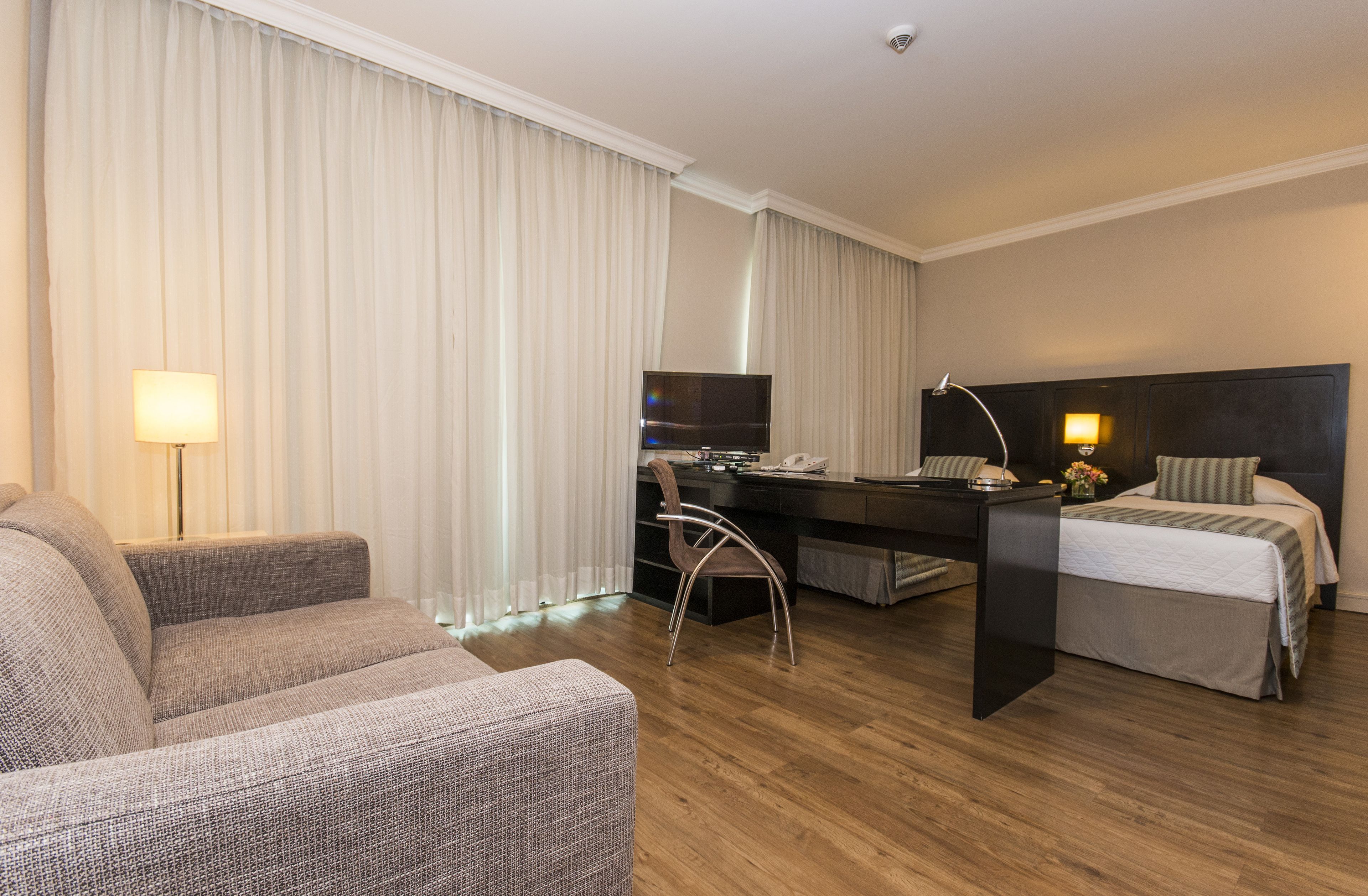 A hotel room with a sofa, a desk with a computer, a bed, and a television.