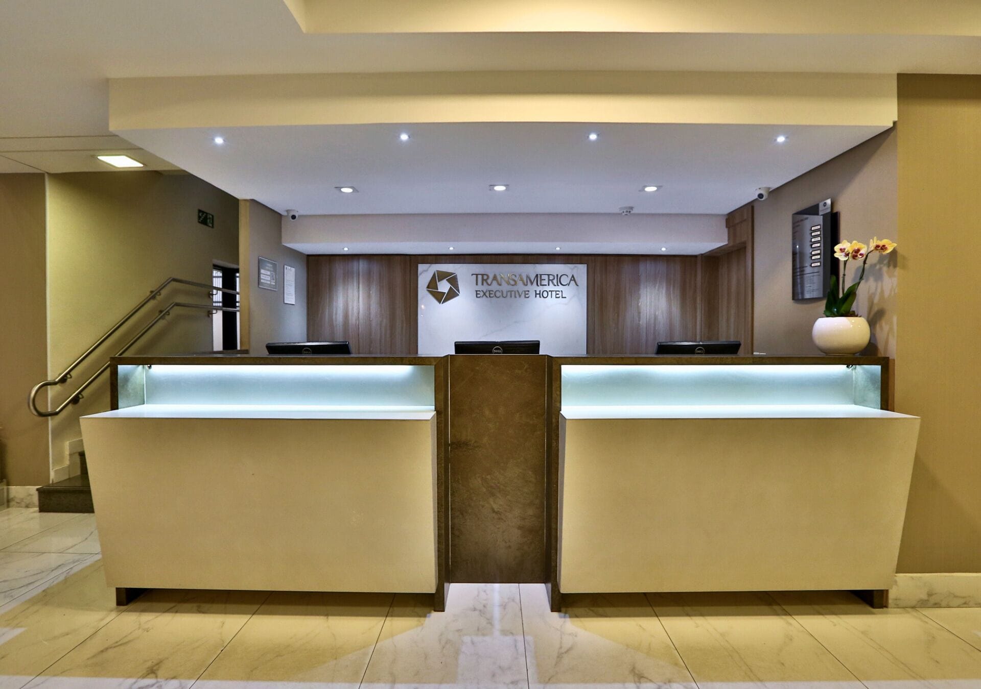 Zona de recepción con mostrador, escalera y cartel del Hotel Ejecutivo Transamerica.