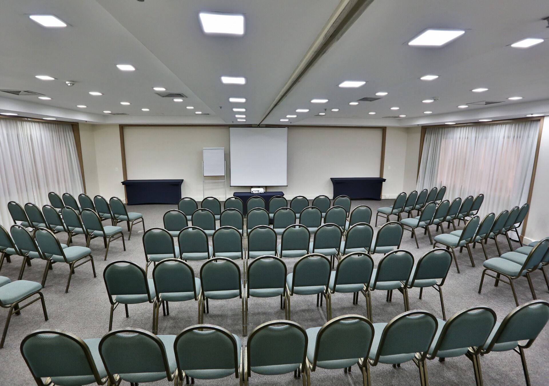Ein Konferenzraum mit Reihen von Stühlen, einer Projektionsleinwand und einer Whiteboard-Tafel.