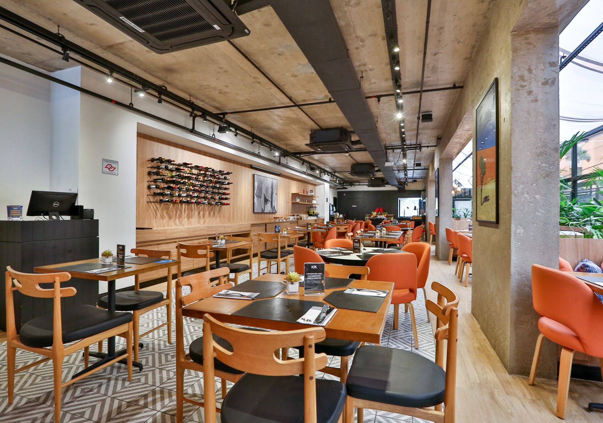 A restaurant with wooden tables and chairs, a wall of wine bottles, and a large window.