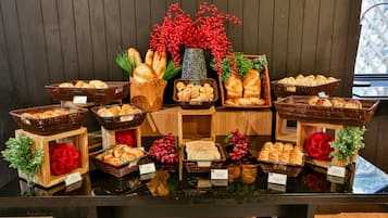 A display of various breads and pastries in baskets and wooden boxes, with some red flowers and greenery for decoration.