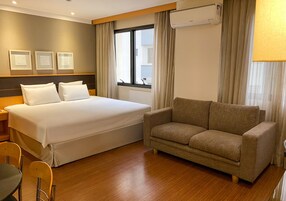 Una camera d'albergo con un letto, una poltrona, una sedia e una finestra con tende.