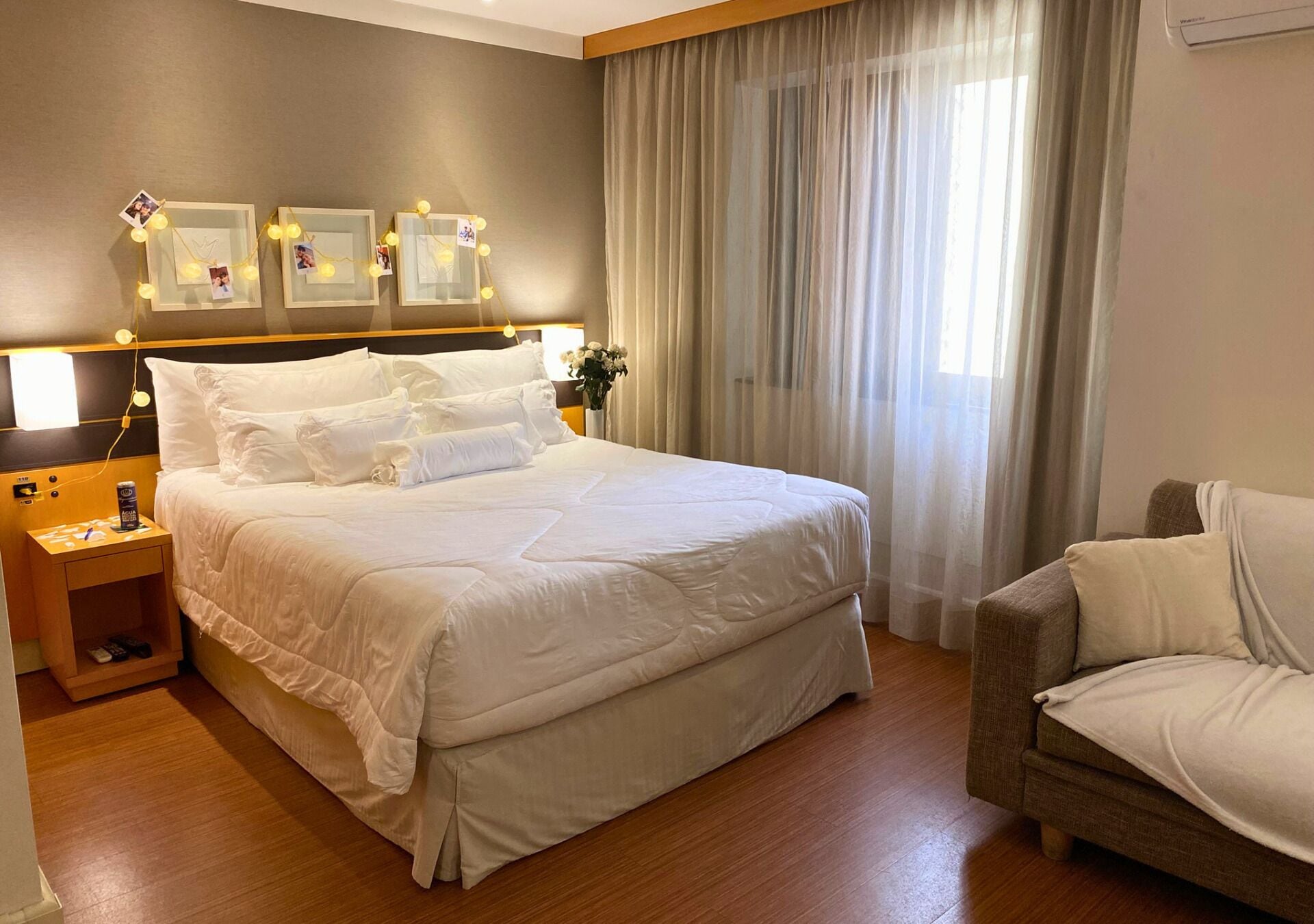 A hotel room with a large bed, a bedside table with a lamp, a chair, and a window with curtains.