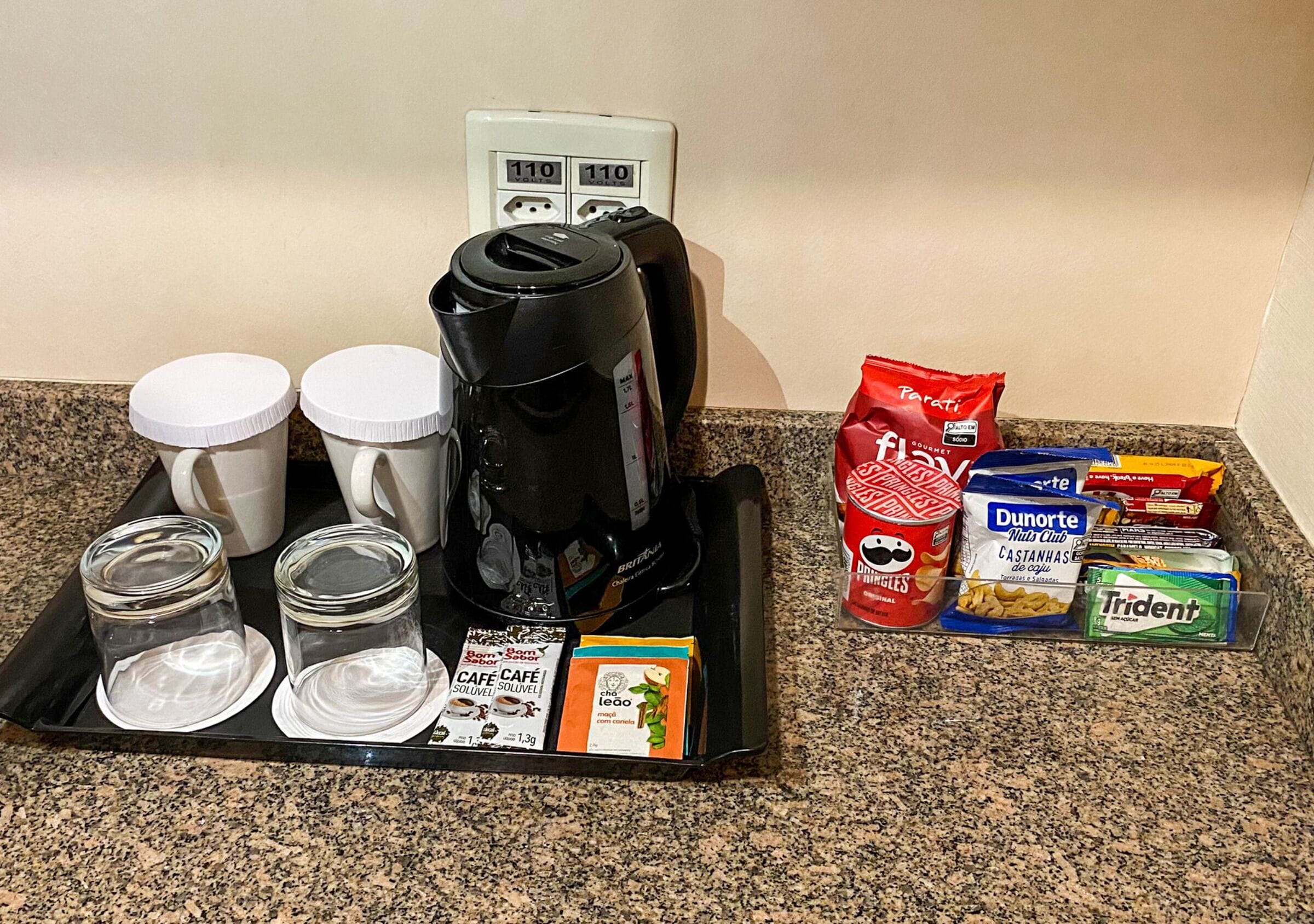 Un comptoir de cuisine avec une machine à café, des tasses, des bocaux et divers aliments, notamment du café en crème et des en-cas.