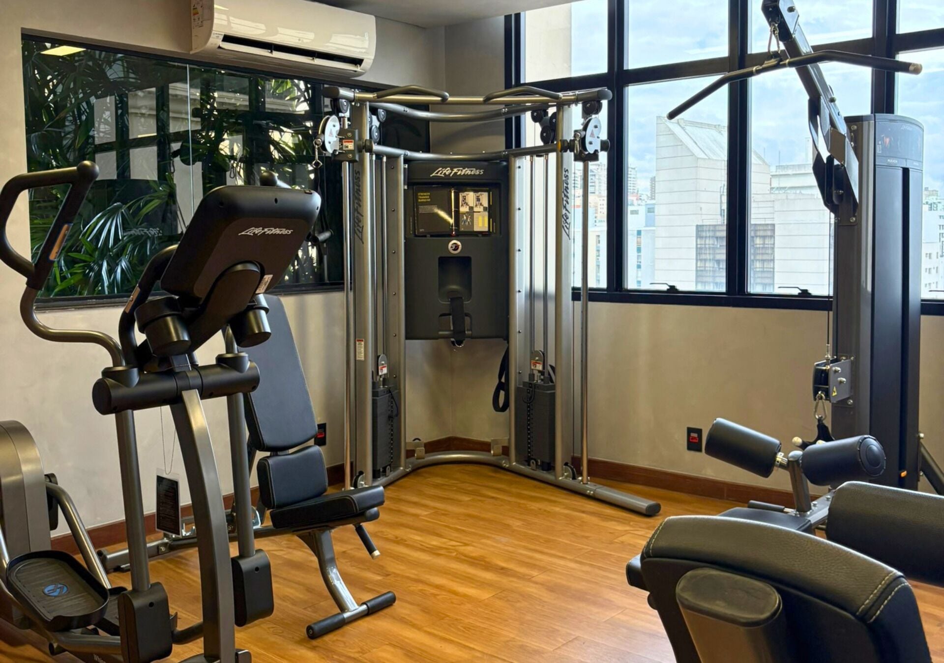 A gym with exercise equipment, large windows, and a wooden floor.