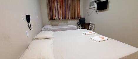 A single bed with white bedding, a telephone, a wall-mounted air conditioner, and a television.