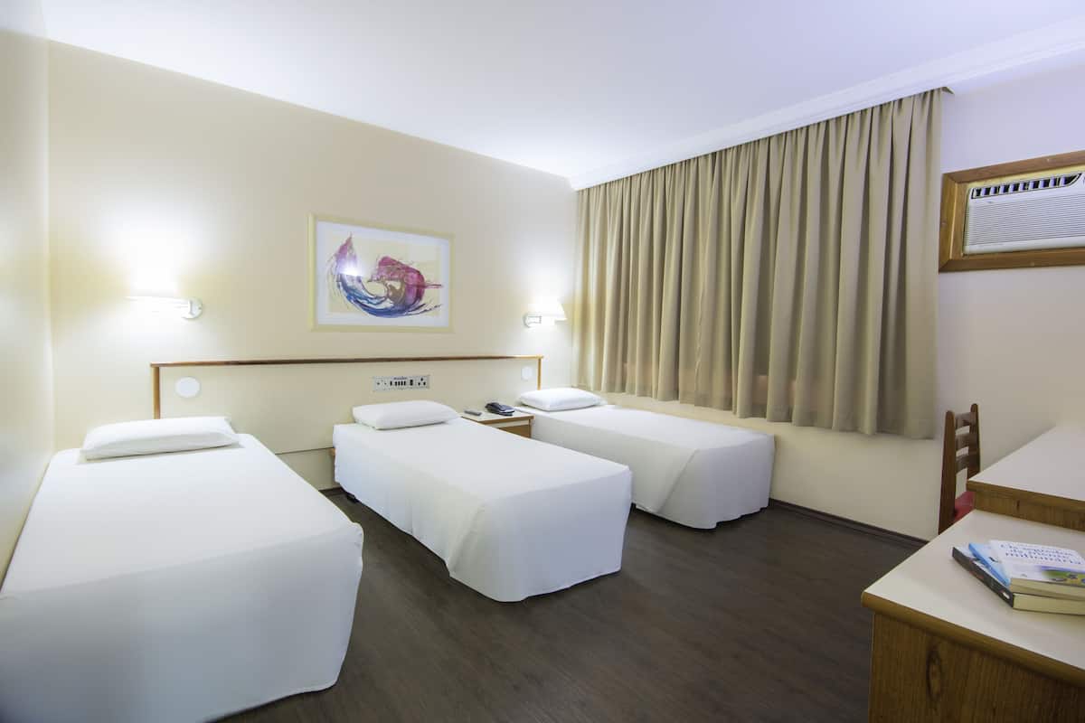 A hotel room with two single beds, a desk, a chair, and a window with curtains.