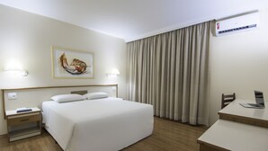 A hotel room with a bed, bedside tables, a desk, a laptop, a painting on the wall, and an air conditioning unit. - Hotel Dan Inn Sorocaba by Nacional Inn (Sorocaba)