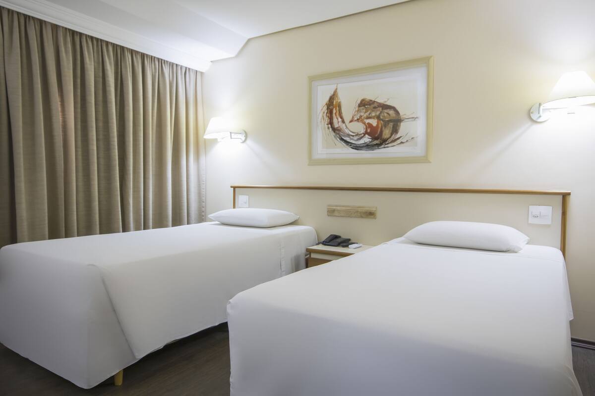 A hotel room with two single beds, a bedside table with a phone, and a painting on the wall.