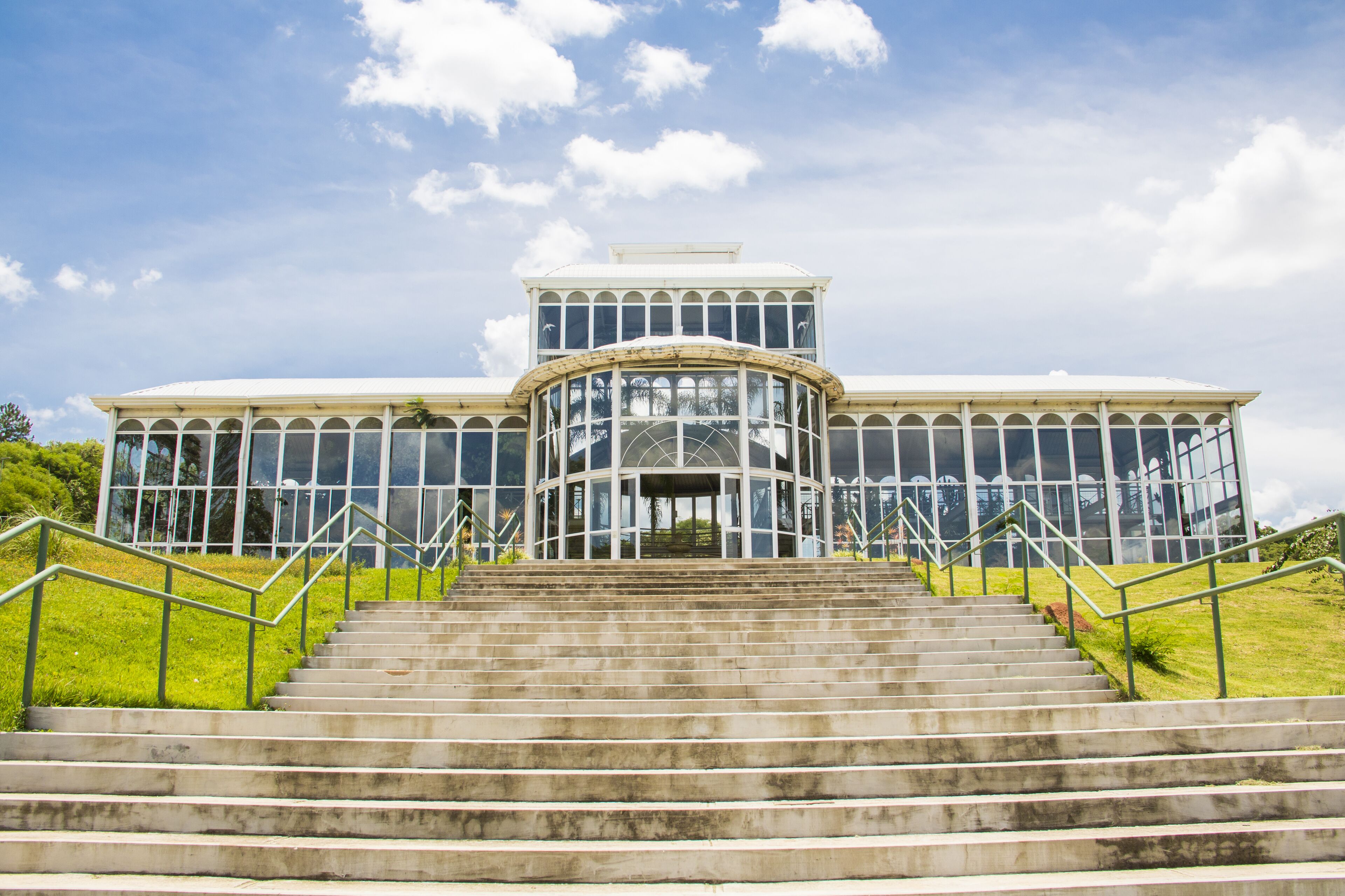 A large building with a glass facade and a central circular section, surrounded by a set of concrete stairs with metal railings.