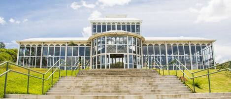 A large building with a glass facade and a central circular section, surrounded by a set of concrete stairs with metal railings.