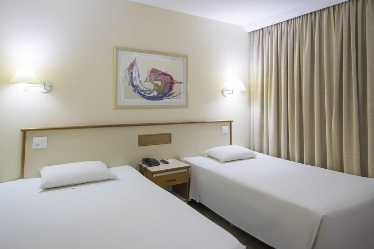 A hotel room with two beds, a nightstand with a phone, and a painting on the wall.