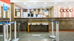 A hotel reception area with a reception desk, computer monitors, and a clock displaying the time. - Hotel Dan Inn Sorocaba by Nacional Inn (Sorocaba)