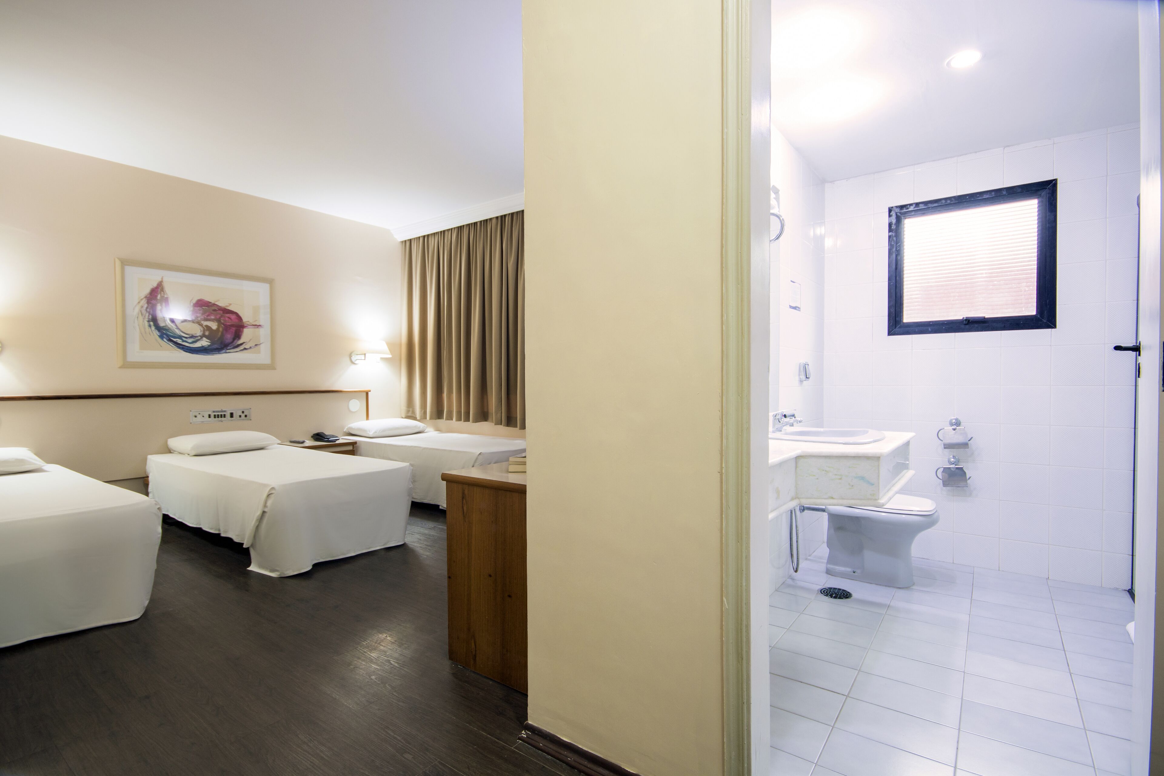 A hotel room with two beds, a wooden nightstand, a painting on the wall, and a bathroom with a sink and toilet.