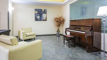 Um hall com piano, sofá, poltrona e um vaso de flores secas.