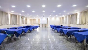 Ein Konferenzraum mit Tischen, Stühlen, einer Projektionsleinwand und einem großen Fenster mit Vorhängen.