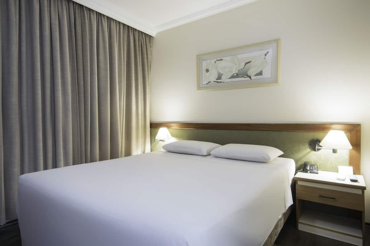 A hotel room with a large bed, two bedside lamps, a nightstand, and a framed picture on the wall.